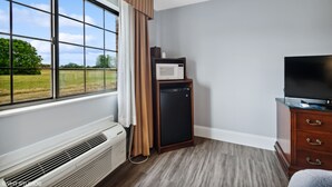 A hotel room with a large window, a built-in air conditioner, a microwave, a television, and a wooden dresser. - My Hometown Inn (Mooresville)