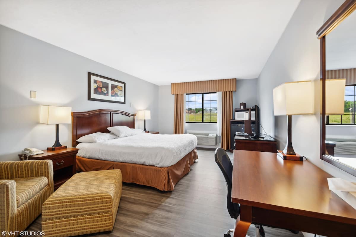 A hotel room with a large bed, two bedside tables with lamps, a desk, a chair, and a window with curtains.