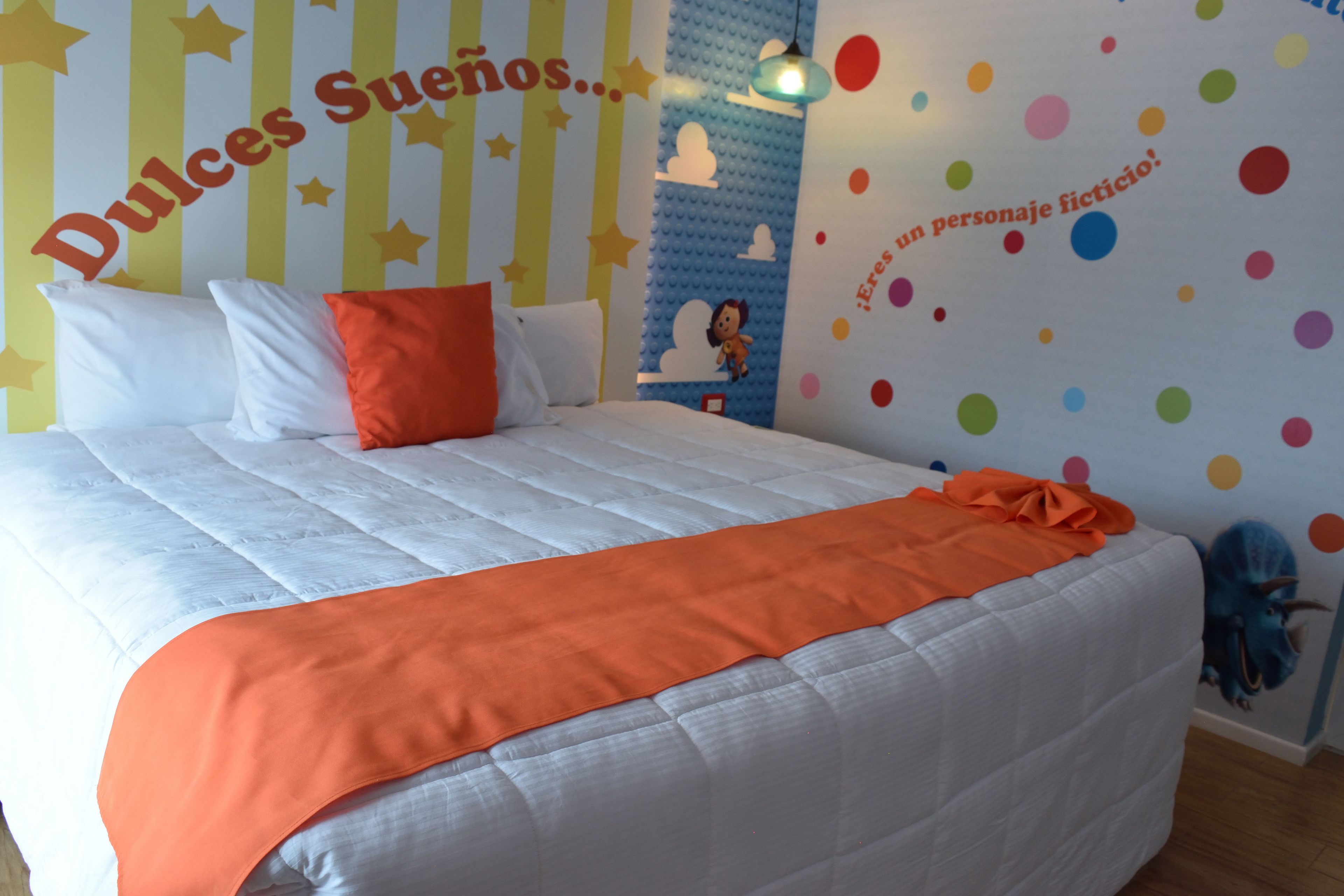 A bed with white bedding and orange accents, a wall with star and cloud decals, and a polka dot pattern.