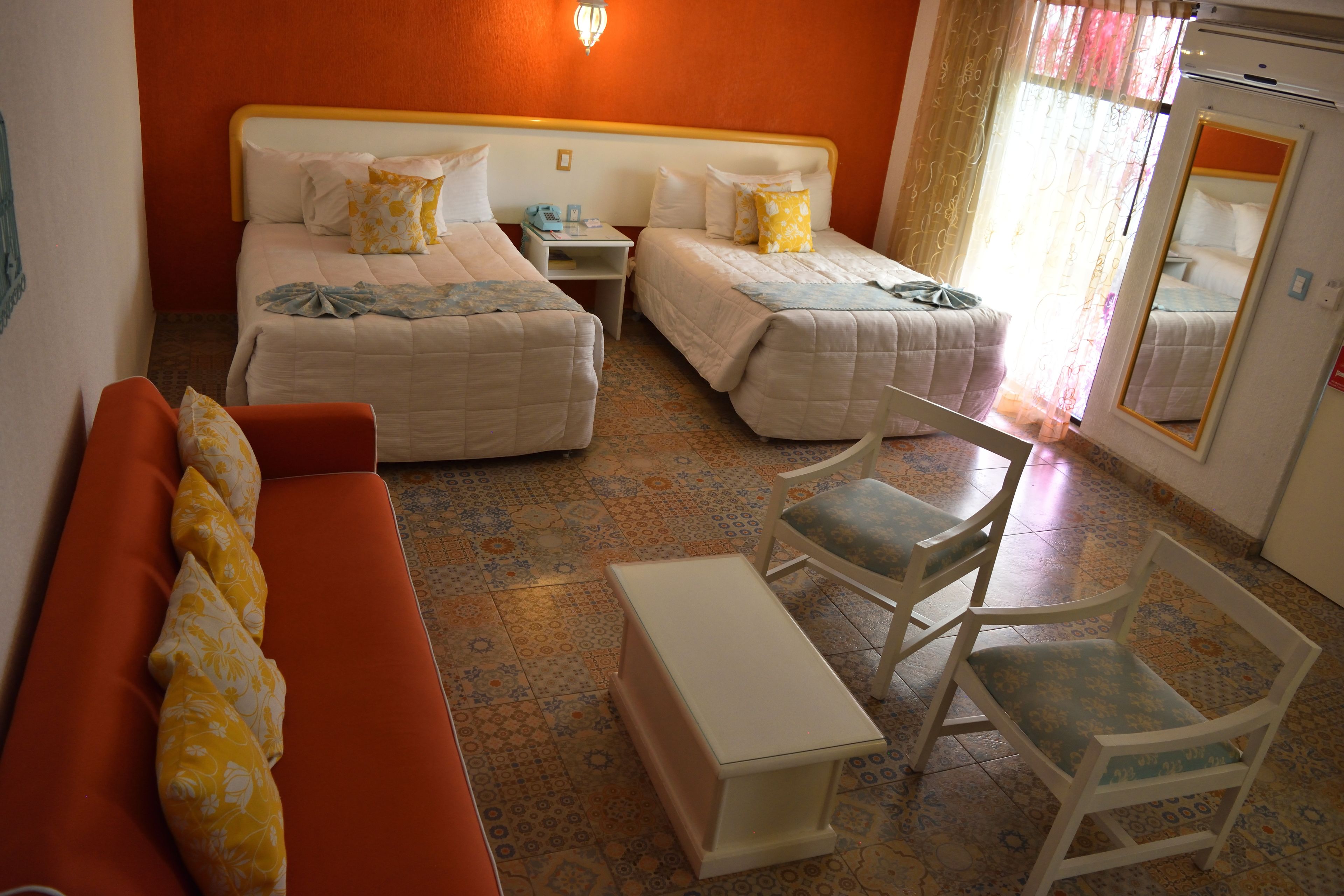 Une chambre d’hôtel avec deux lits, un canapé, une chaise, une petite table et un miroir.