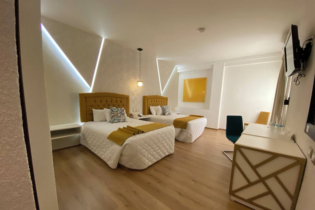 Una habitación de hotel moderna con dos camas, piso de madera y un espejo grande.