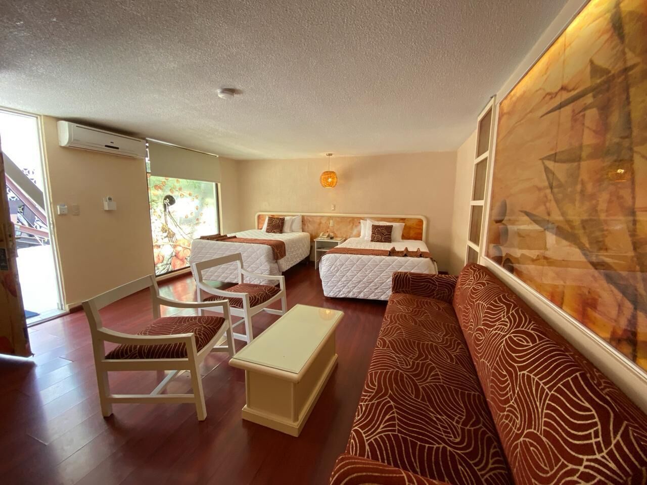 A hotel room with two beds, a sofa, a chair, a small table, and a large window.