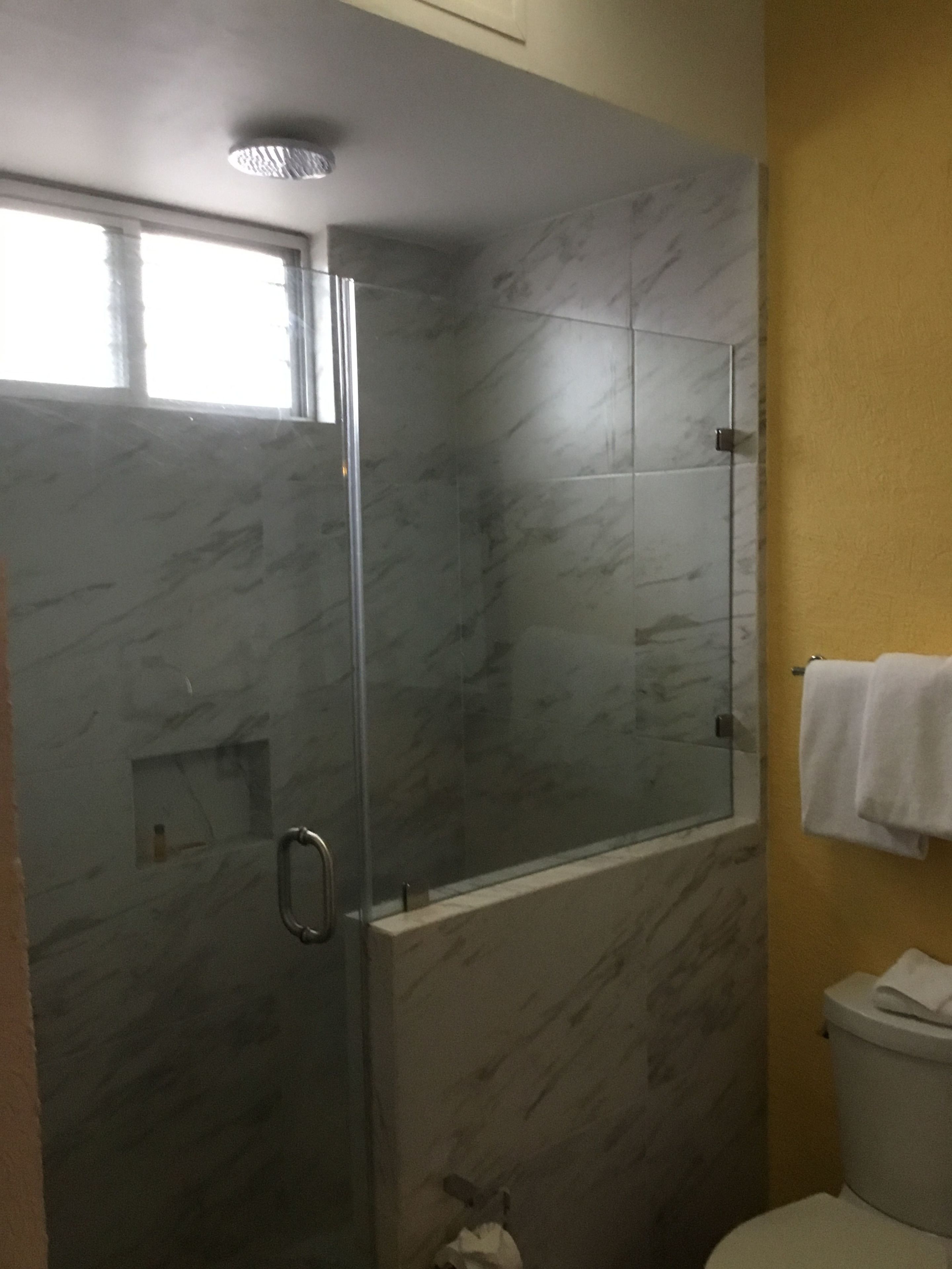 A bathroom with a glass-enclosed shower, marble walls, a toilet, and a towel rack.