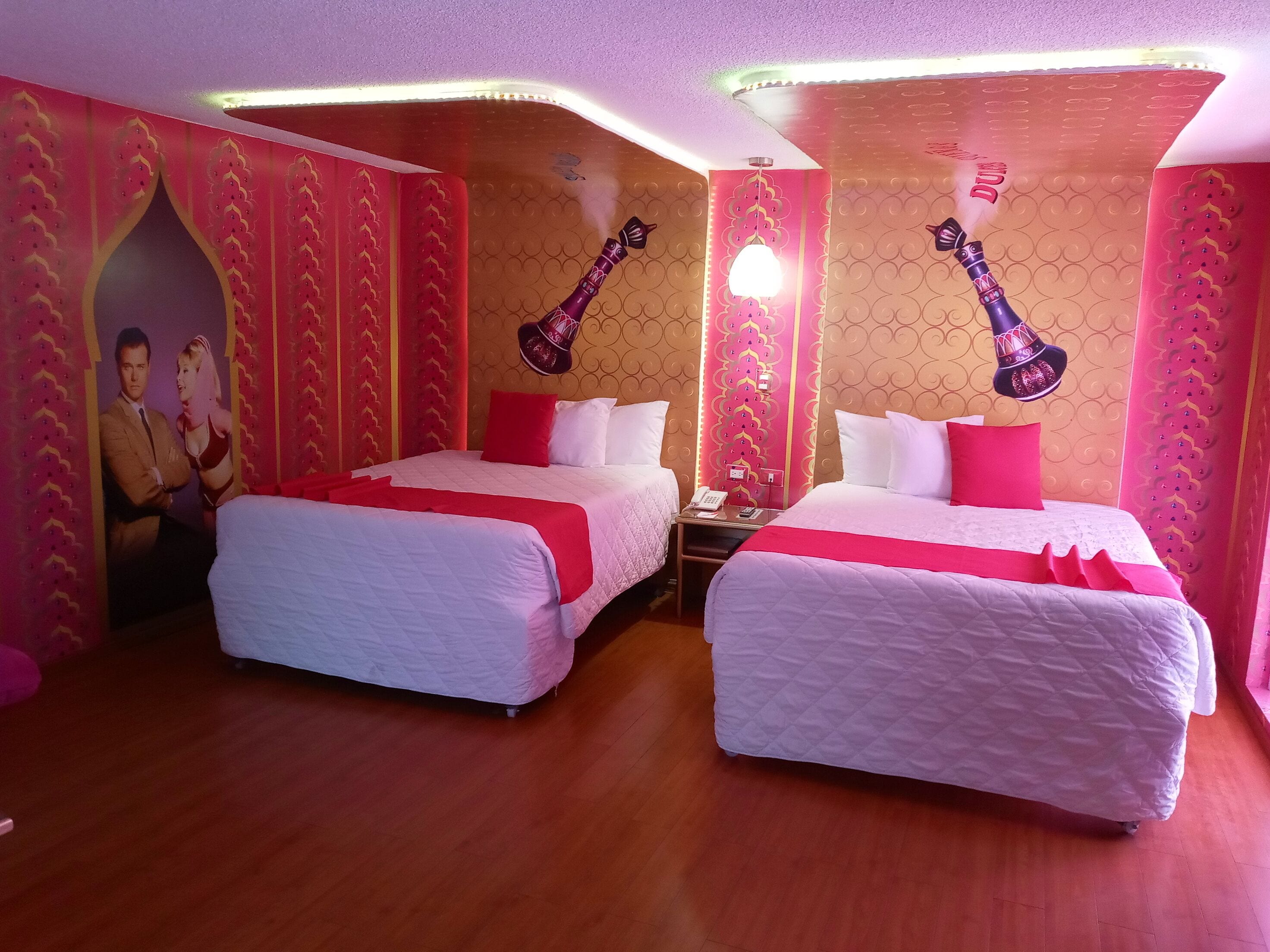 A hotel room with two beds, red and white bedding, a poster on the wall, and a telephone on the nightstand.
