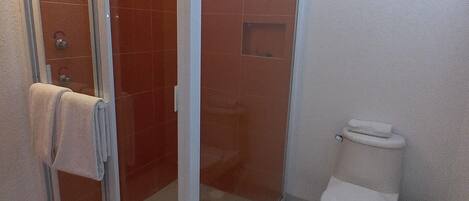 Un baño con mampara de vidrio, inodoro y una ventana pequeña.