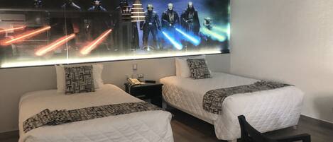 Een hotelkamer met twee bedden, een nachtkastje, een stoel en een grote televisie waarop een film te zien is.