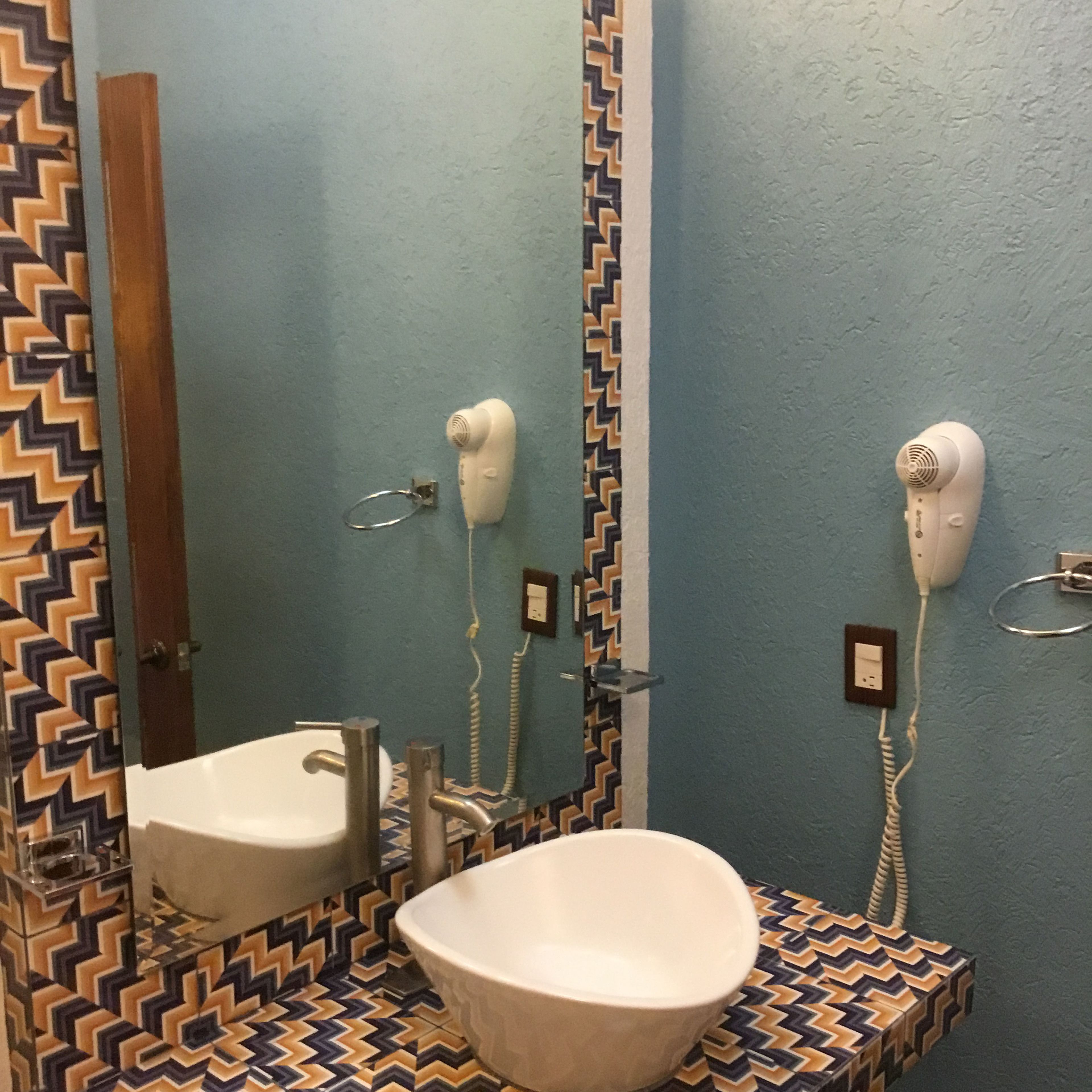 A bathroom with a zigzag patterned tile floor, a white sink, and two hair dryers mounted on the wall.
