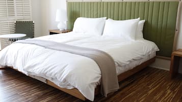 A neatly made bed with white linens and a grey throw blanket, a green upholstered headboard, and a wooden floor.