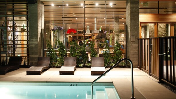 Un espace piscine doté de chaises longues, d’un mur de verre agrémenté de plantes et d’un aménagement intérieur moderne.