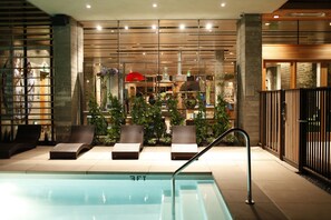 A swimming pool area with lounge chairs, a glass wall with plants, and a modern interior design. - H2Hotel (Healdsburg)