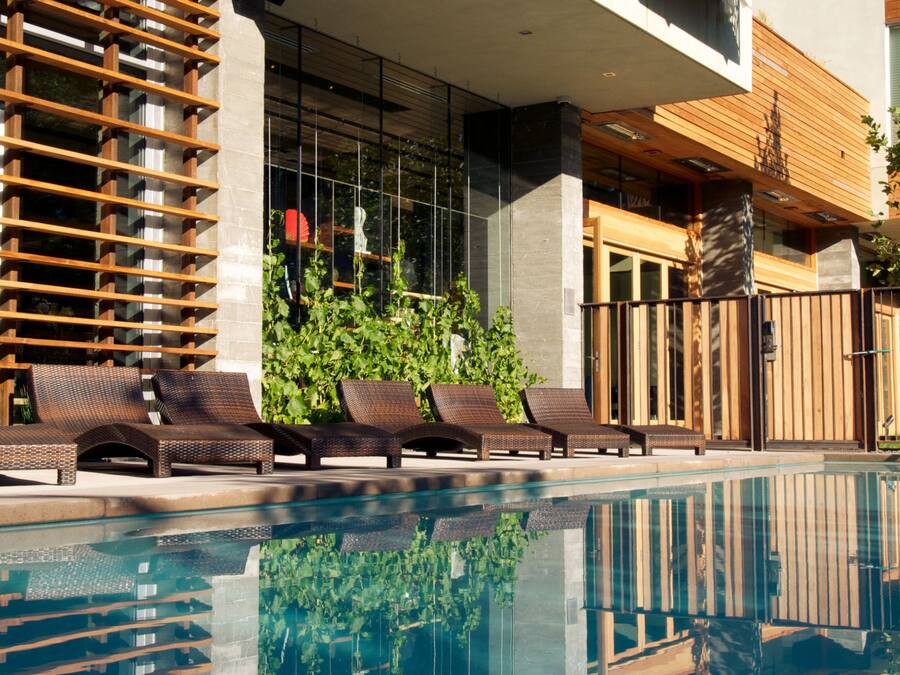 Un hotel moderno con piscina, mobiliario exterior y balcón de madera.