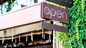 Un bar avec une enseigne indiquant qu’il est ouvert, des tables en terrasse et une enseigne « Spoonbar ».