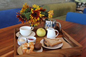 Una bandeja de madera con alimentos para el desayuno, como pan, pasteles y una jarra de leche, colocada sobre una mesa con un jarrón de girasoles al fondo.