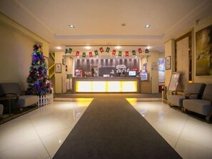 Zona de recepción de un hotel con un mostrador, sillas, un árbol de Navidad y una pared con banderas.