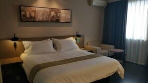 A hotel room with a large bed, a small table, a chair, a wall-mounted air conditioner, and a painting above the bed. - Jinjiang Inn Changchun Exhibition Center (Changchun)