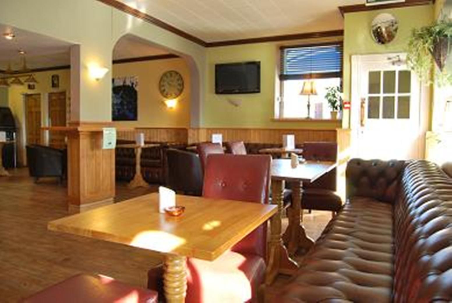 A restaurant with wooden tables and booths, a leather couch, and a clock on the wall.