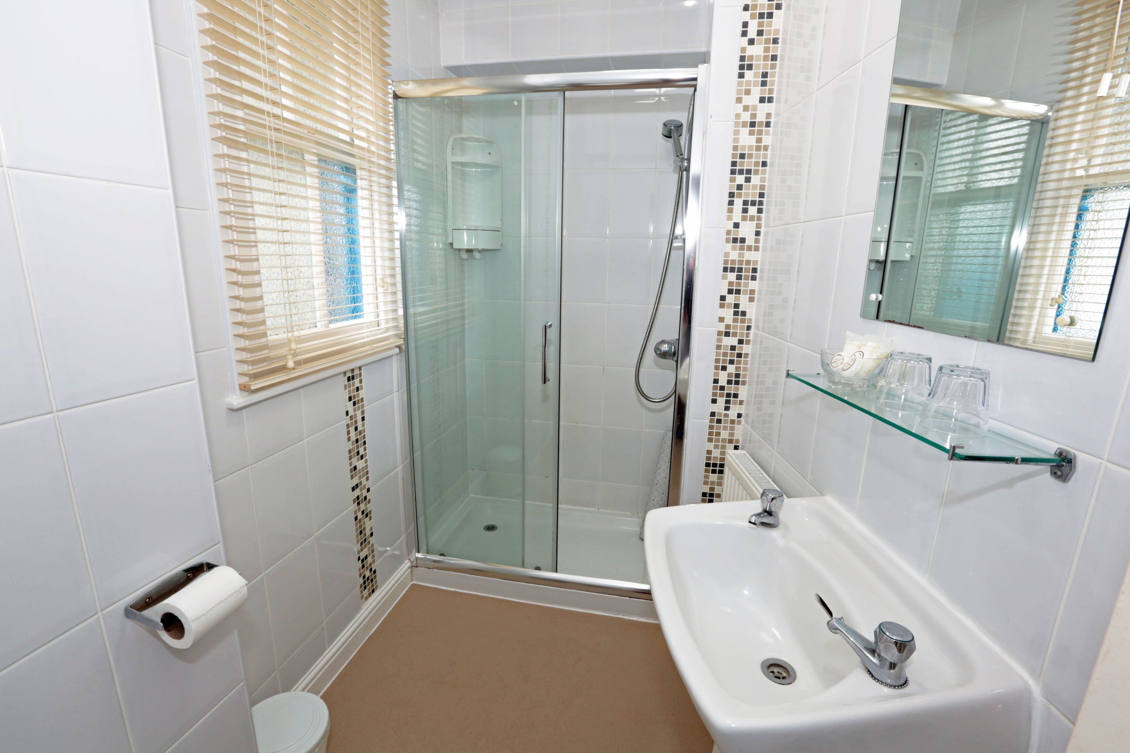 A modern bathroom with a glass-enclosed shower, a white sink, and a glass shelf.