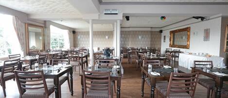 A spacious dining area with multiple tables and chairs, high ceilings with textured patterns, and large windows allowing natural light.