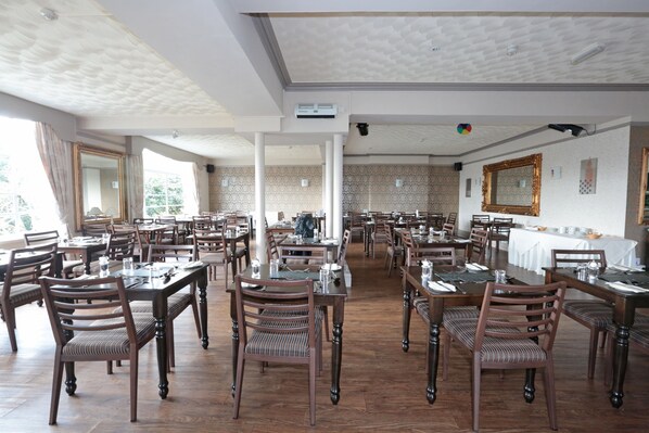 A spacious dining area with multiple tables and chairs, high ceilings with textured patterns, and large windows allowing natural light. - Lion Hotel and Studio Apartments (Criccieth)