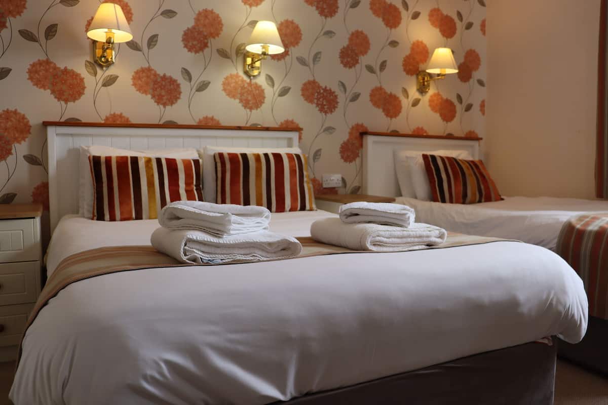 Ein Hotelzimmer mit zwei Betten, jeweils mit weißen Laken und gestreiften Kissen. An beiden Seiten der Betten befinden sich Wandlampen.