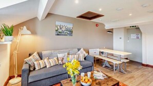 A modern living room with a grey sofa, a wooden coffee table with a vase of flowers, and a white table with benches.