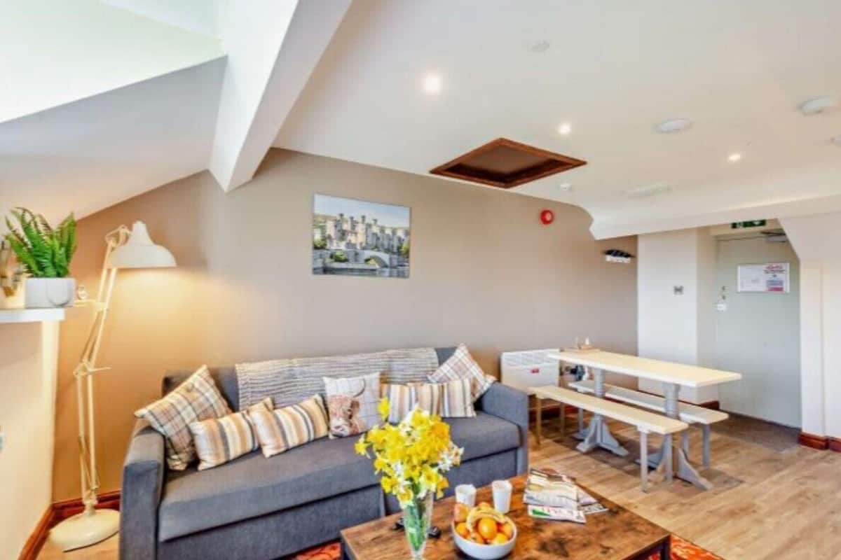Ein modernes Wohnzimmer mit einem grauen Sofa, einem Holztisch mit Blumenvase und einem weißen Tisch mit Bänken.