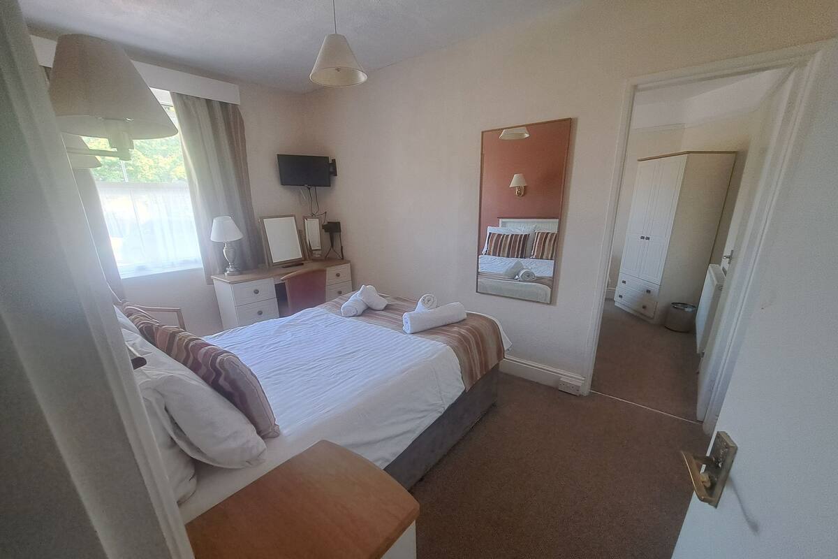 Ein Hotelzimmer mit Bett, Nachttisch, Schreibtisch, Stuhl und einem an der Wand befestigten Fernseher.