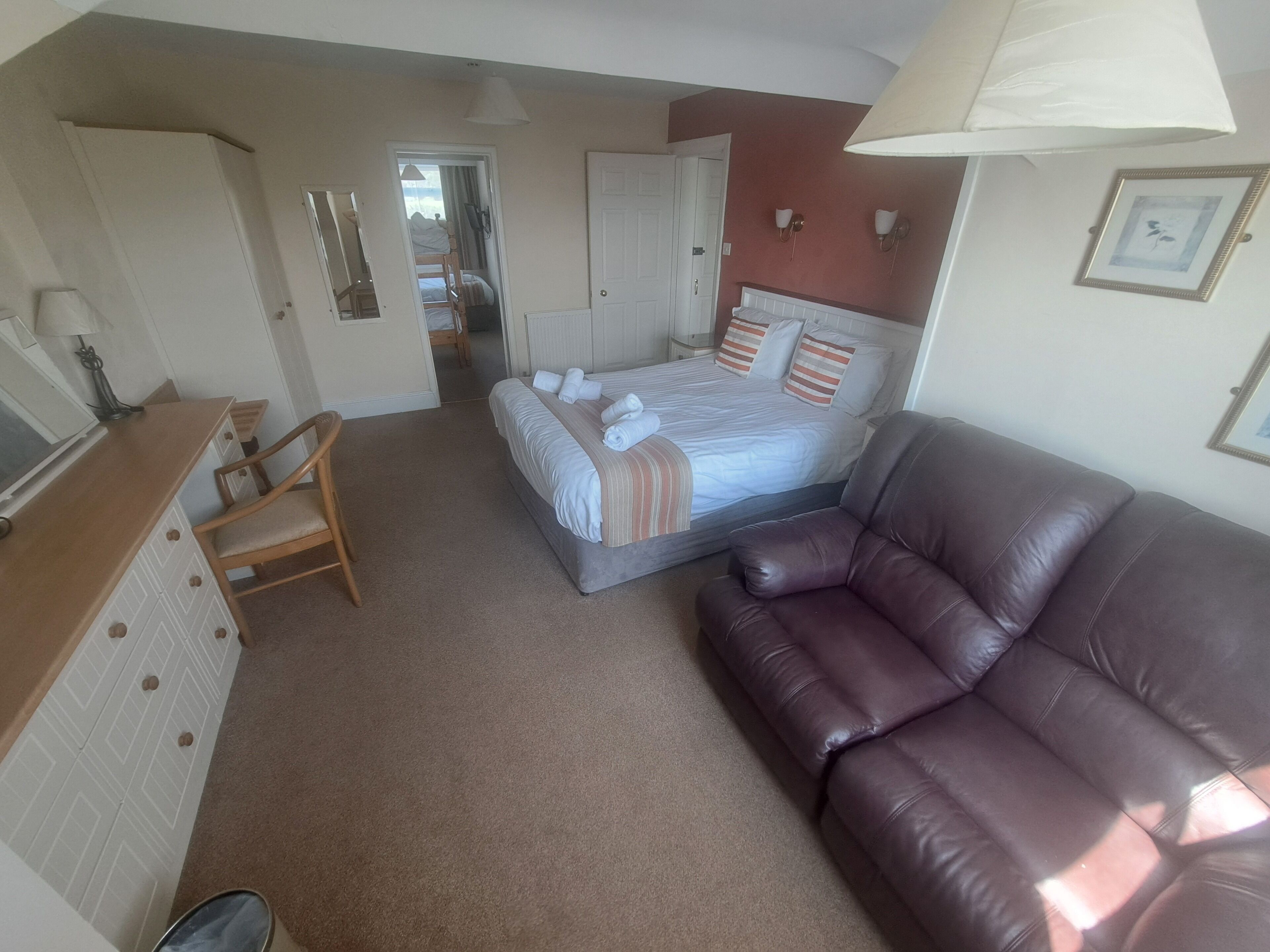 A bedroom with a bed, a brown leather sofa, a wooden desk, and a chair.