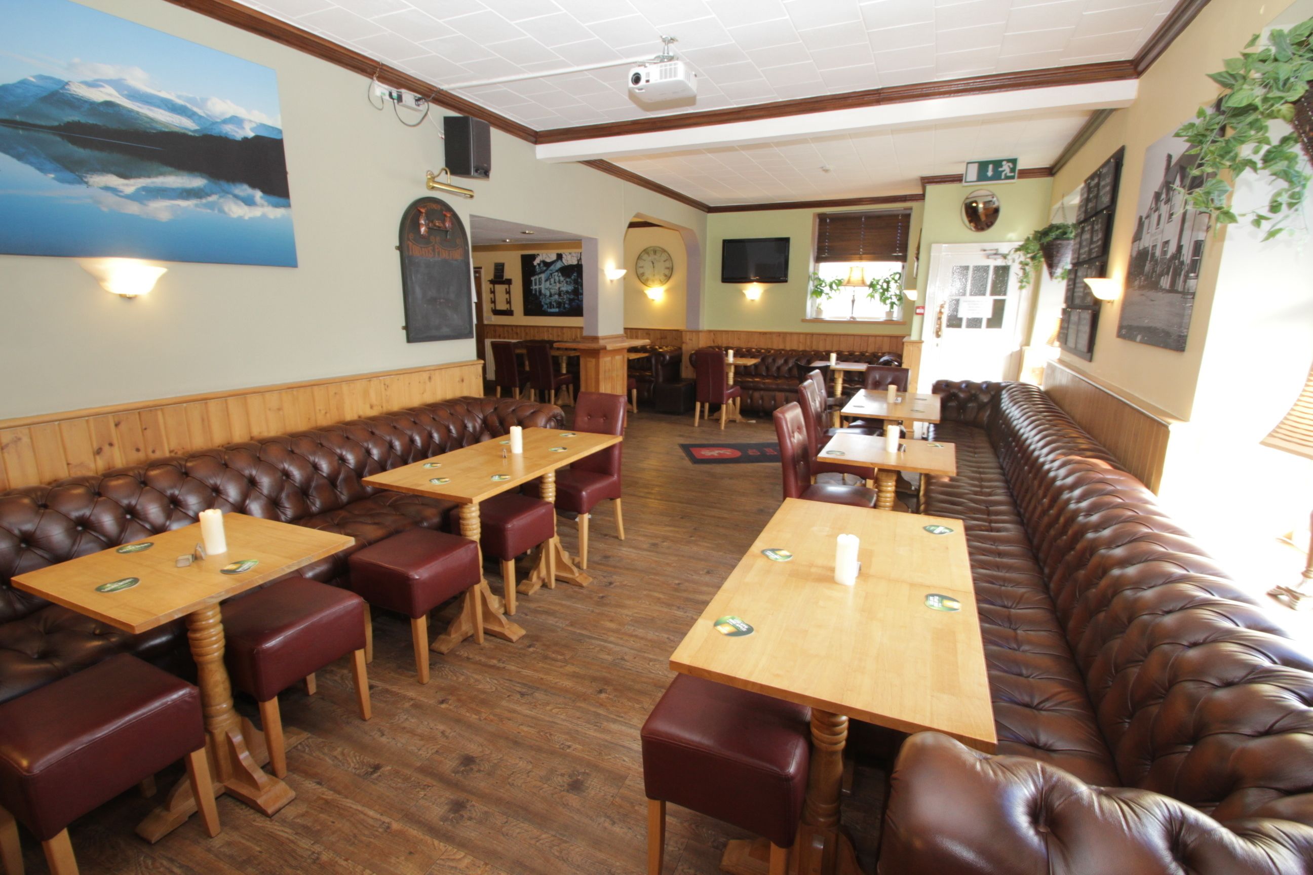 Un restaurant avec des tables et des banquettes en bois, une scène et un grand tableau accroché au mur.