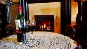 A table with a bottle of wine and two glasses, a fireplace in the background, and a patterned tablecloth.
