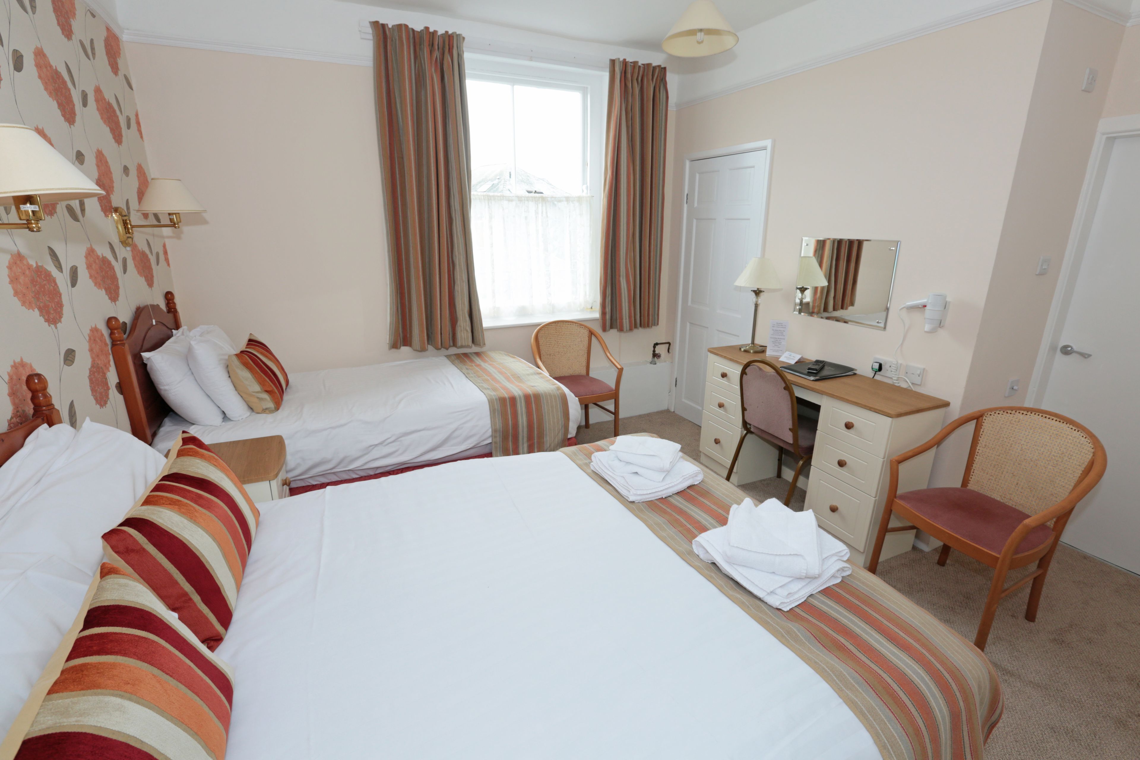 A hotel room with two beds, a desk, a chair, and a window with curtains.