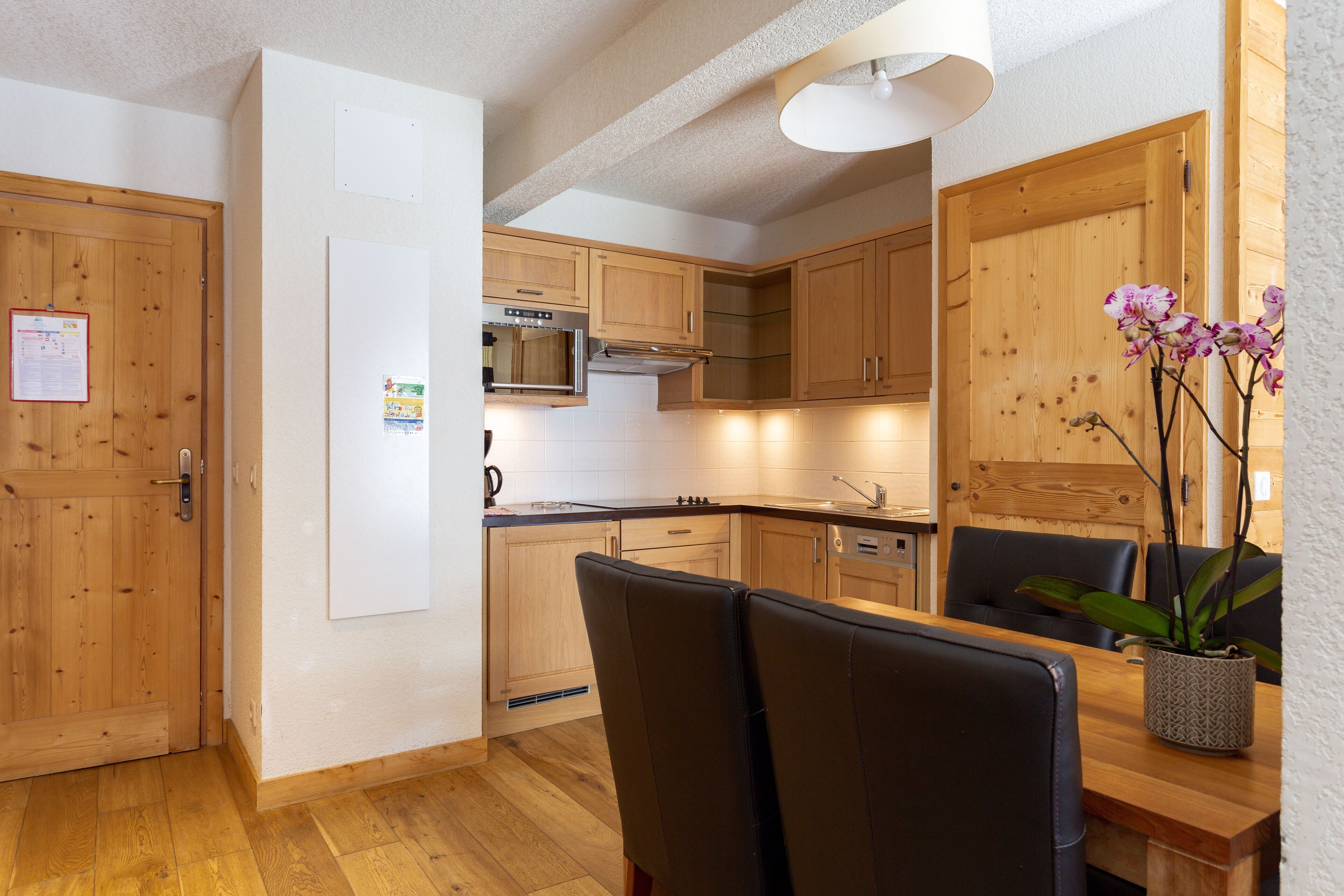 Eine moderne Küche mit Holzschränken, einem Einbauofen und einem Essbereich mit zwei Stühlen und einem Tisch.