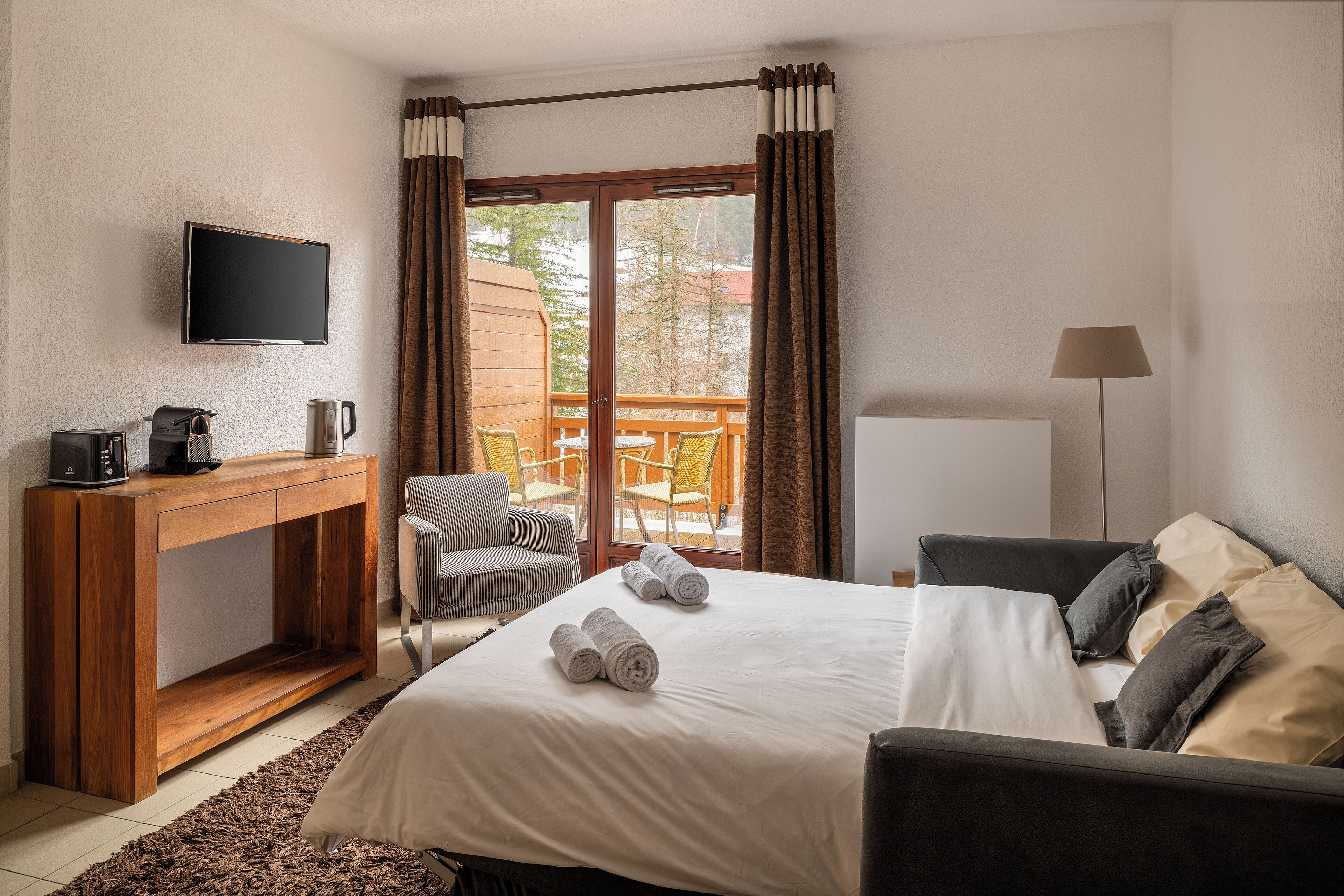 Une chambre d’hôtel équipée d’un lit, d’un bureau avec une machine à café, d’une télévision et offrant une vue sur l’extérieur.