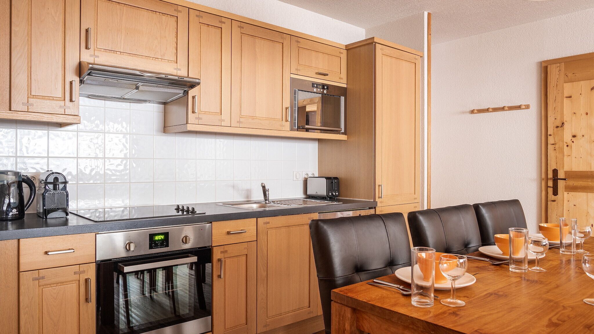 Een moderne keuken met houten kastjes, een rvs fornuis, een magnetron, en een eetgedeelte met een houten tafel en leren stoelen.
