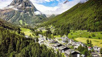 Un pueblo montañoso con un pico destacado, un bosque denso y un pequeño asentamiento con edificios y caminos.