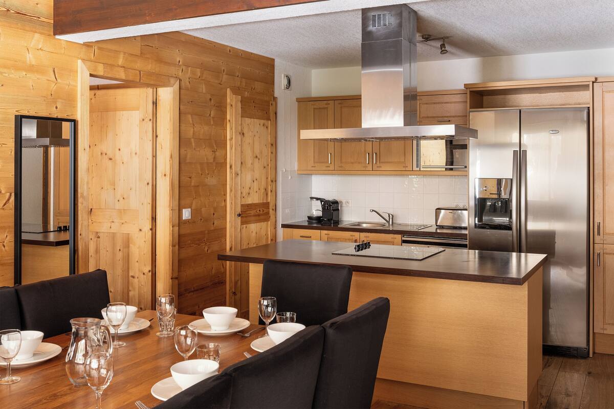 A modern kitchen with wooden cabinetry, stainless steel appliances, and a dining area with a table set for four.