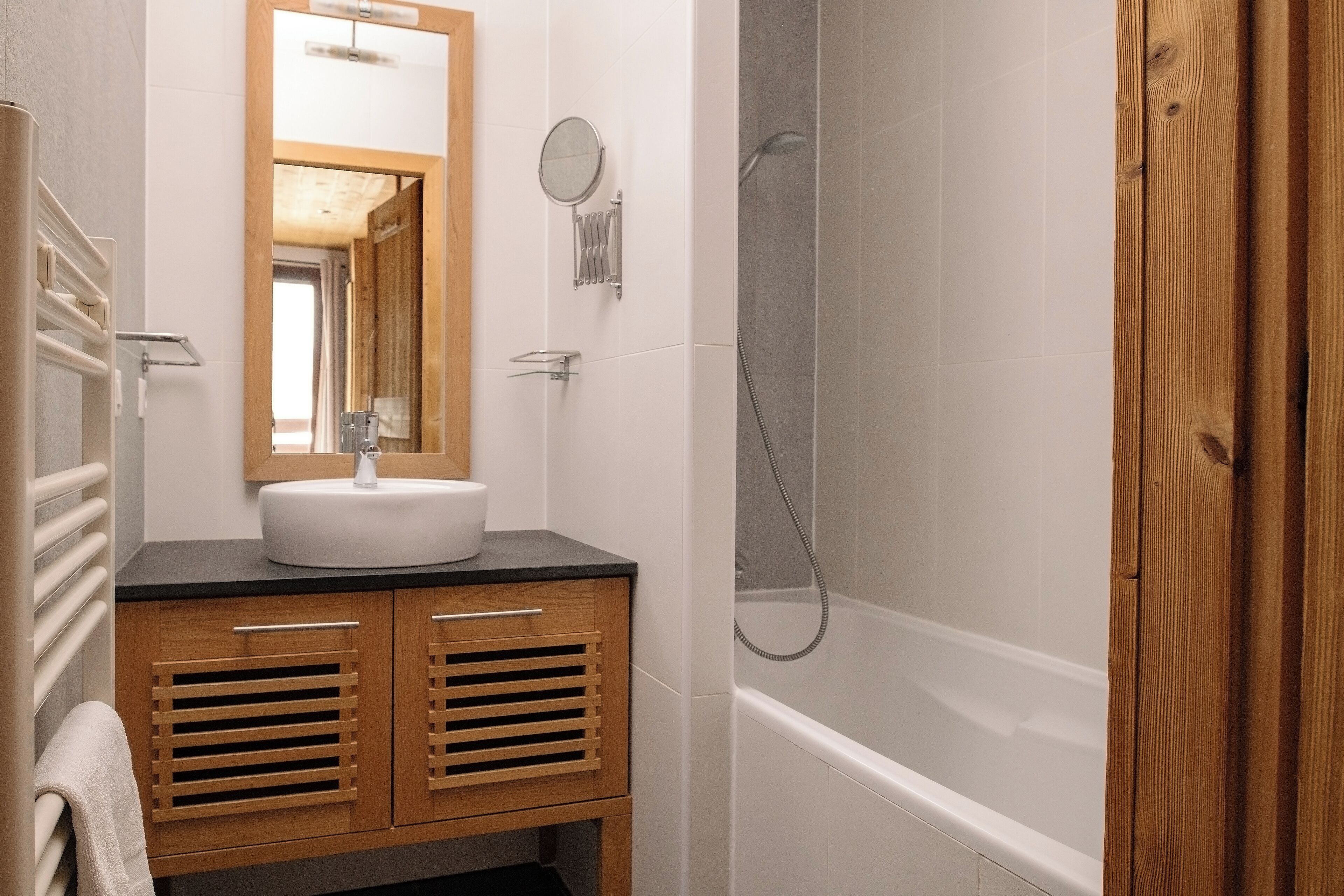 A bathroom with a wooden vanity, a sink, a mirror, and a shower area.