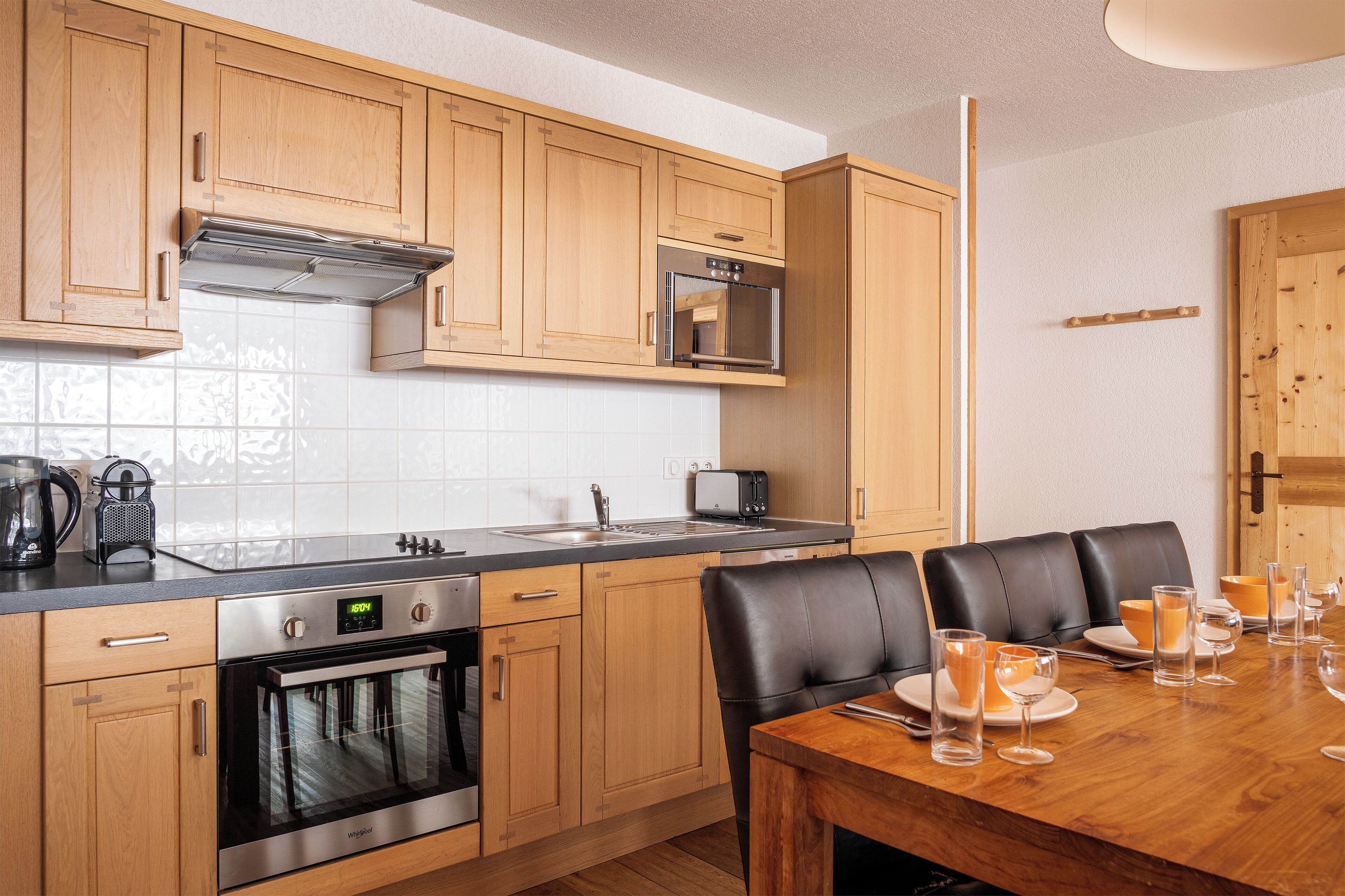 Une cuisine moderne avec des meubles en bois, des appareils en acier inoxydable et un coin repas avec une table dressée pour quatre personnes.