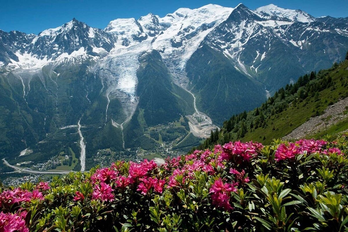 A mountain landscape with snow-capped peaks, a glacier, and a valley with a road.