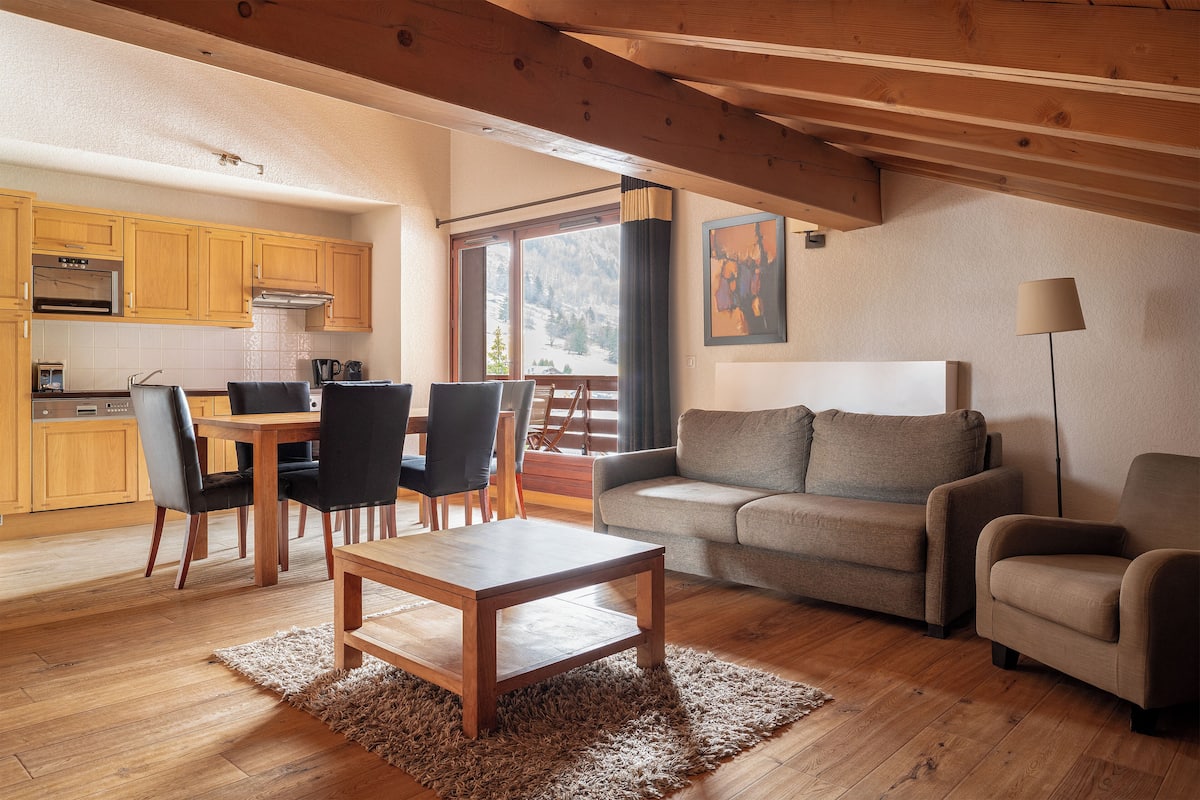 A cozy living area with a wooden dining table, chairs, a sofa, and a lamp.