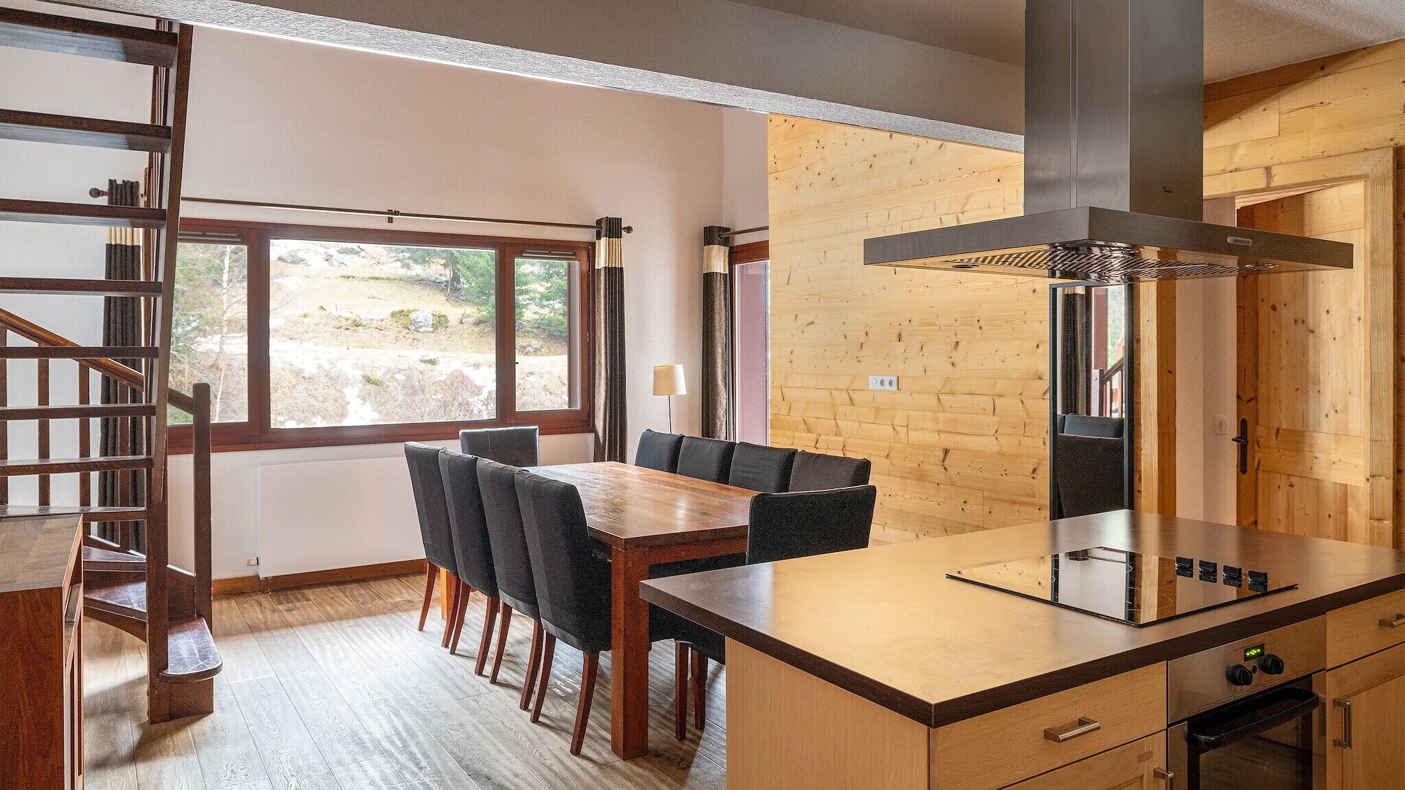 A modern kitchen with a wooden island, built-in stove, and a dining area with a wooden table and chairs.