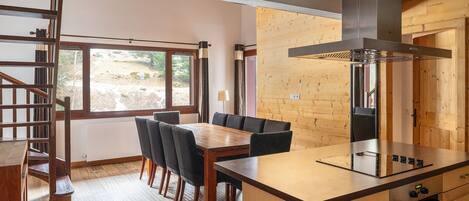 A modern kitchen with a wooden island, built-in stove, and a dining area with a wooden table and chairs.