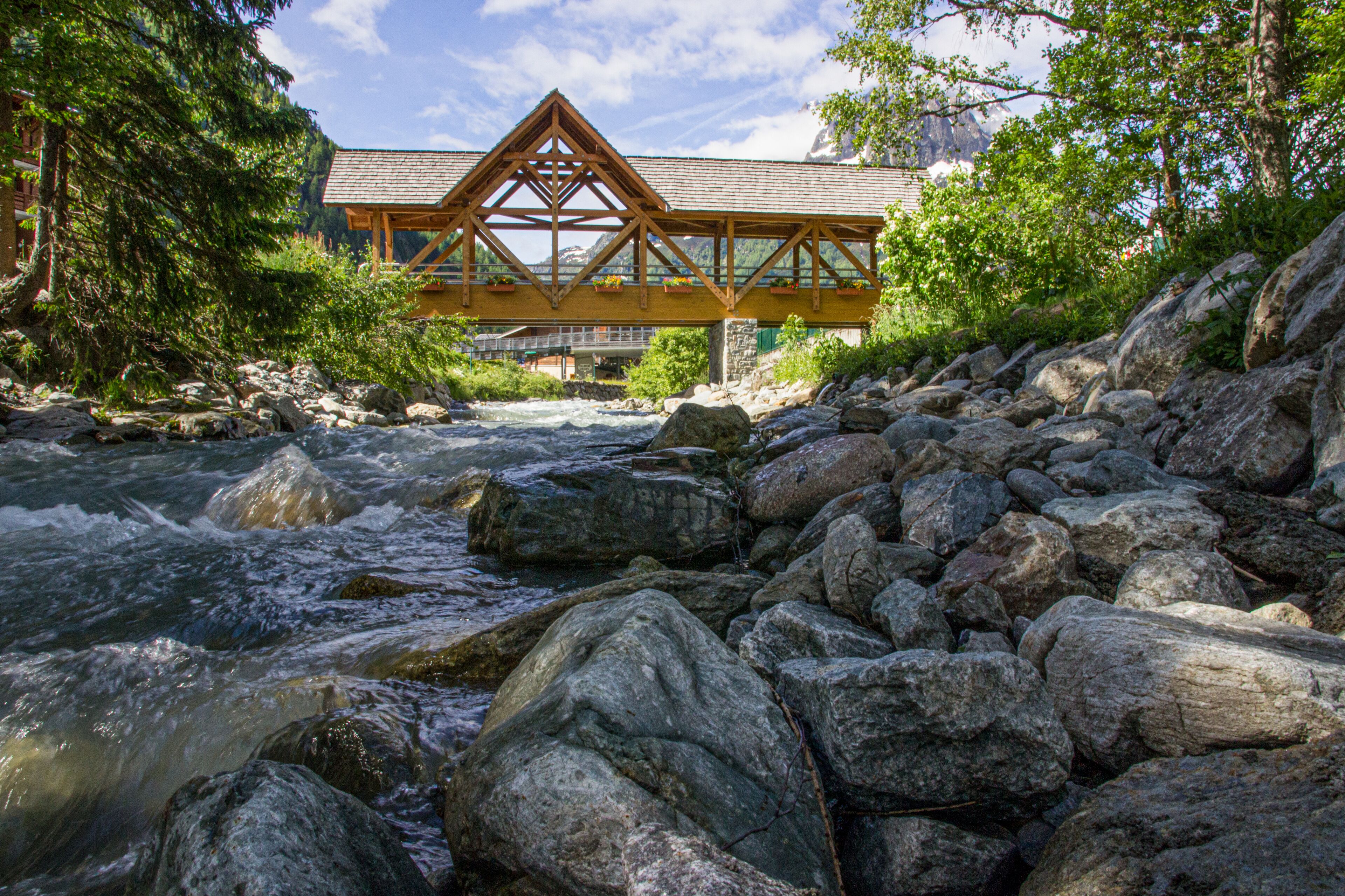 Un pont en bois enjambe une rivière, avec de gros rochers au premier plan.