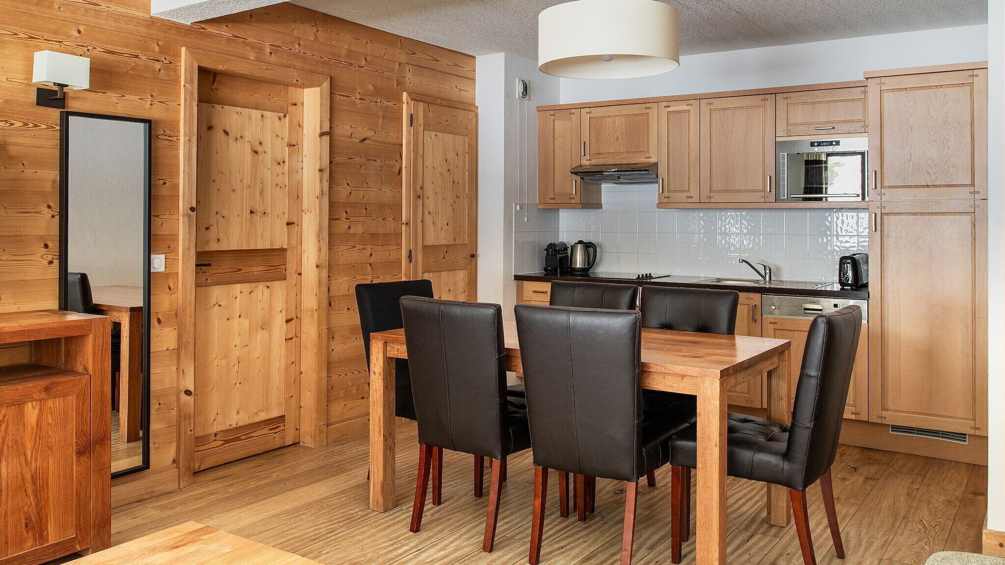 Una cocina moderna con armarios de madera, una mesa de comedor con sillas y un horno empotrado.