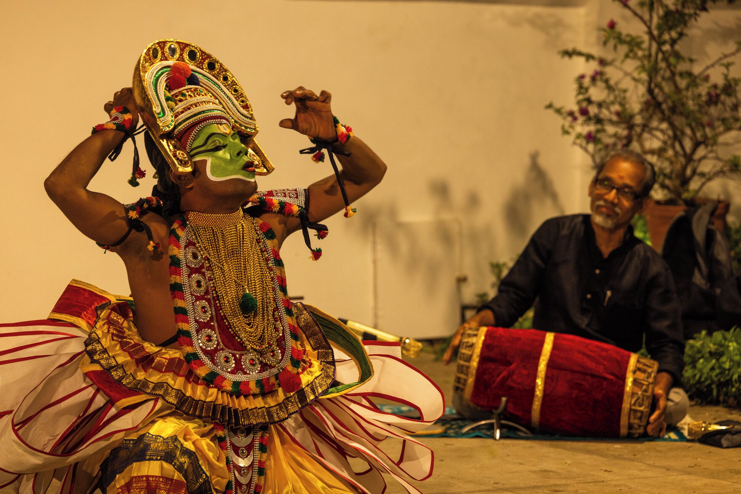 A person in traditional attire performing on a stage with a seated audience.