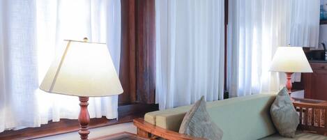 A room with a wooden sofa, two lamps, and curtains.
