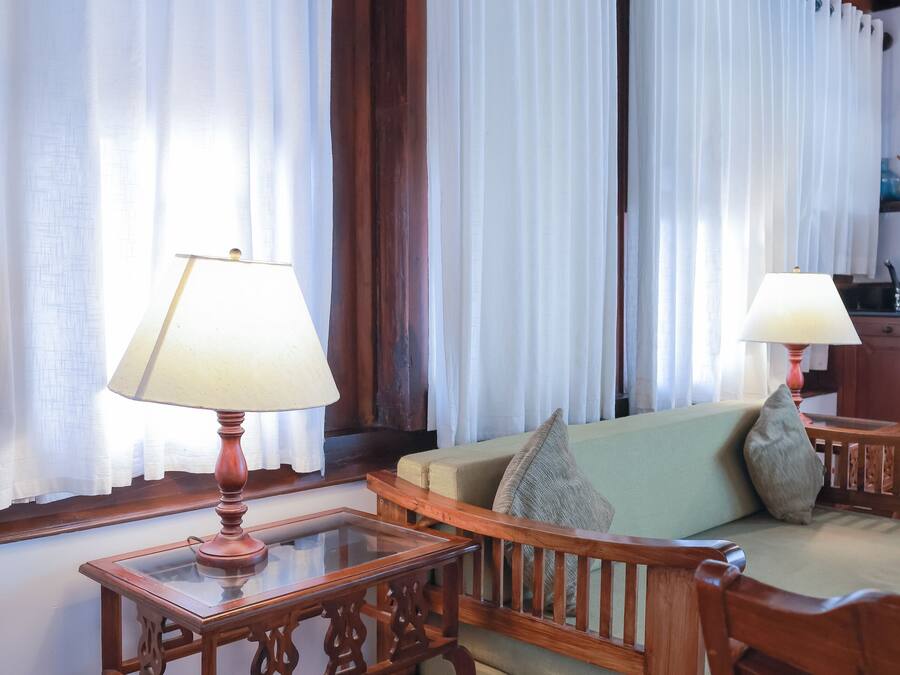 A room with a wooden sofa, two lamps, and curtains.