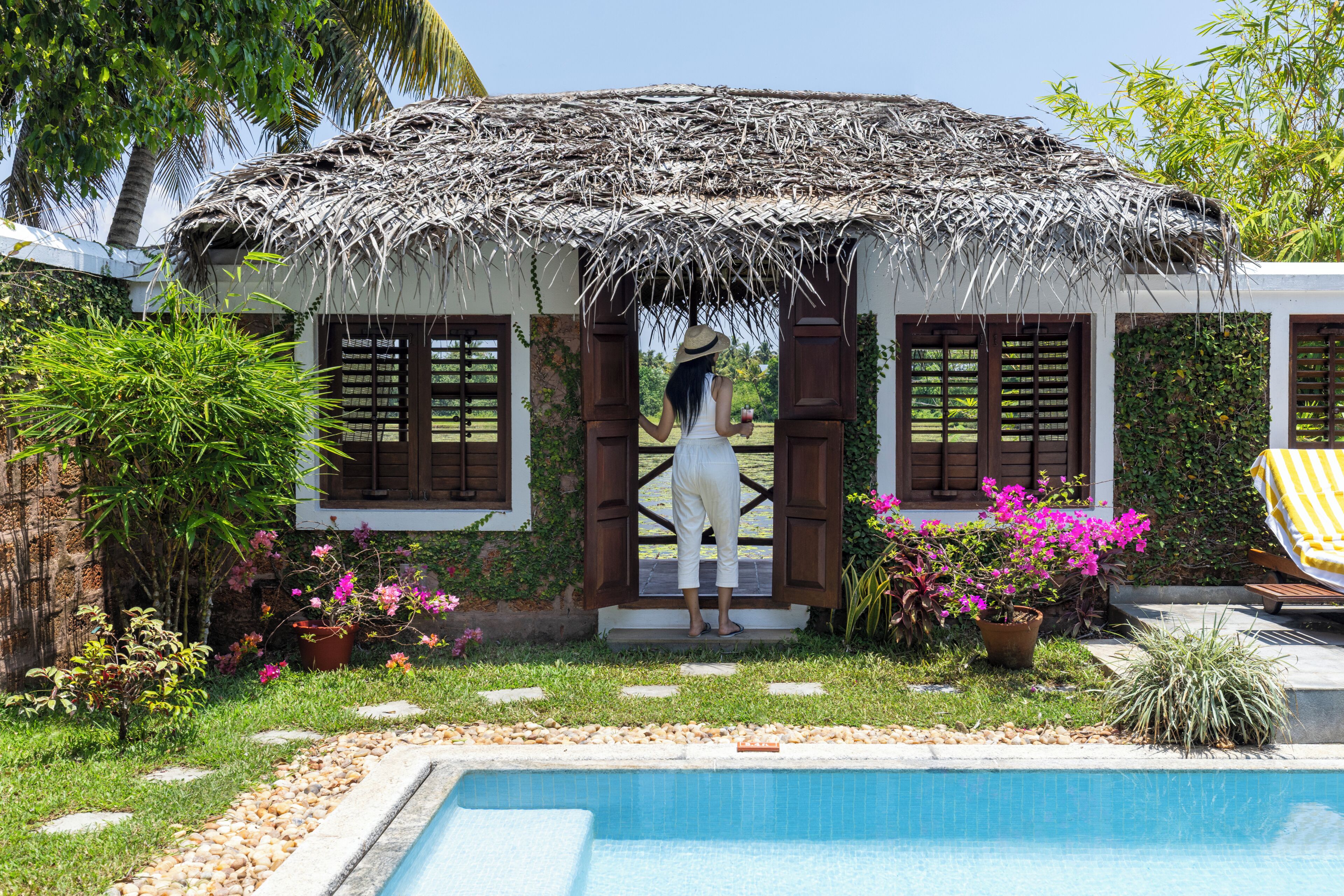 A pool area with a thatched structure, a pool, and surrounding greenery.