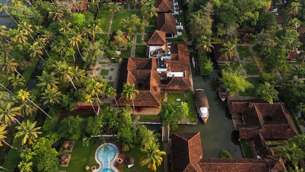 Vista aérea de un resort con varias construcciones tipo bungaló, una piscina y exuberante vegetación circundante.