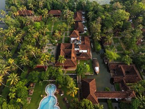 An aerial view of a resort with multiple bungalow-style buildings, a swimming pool, and surrounding lush greenery.